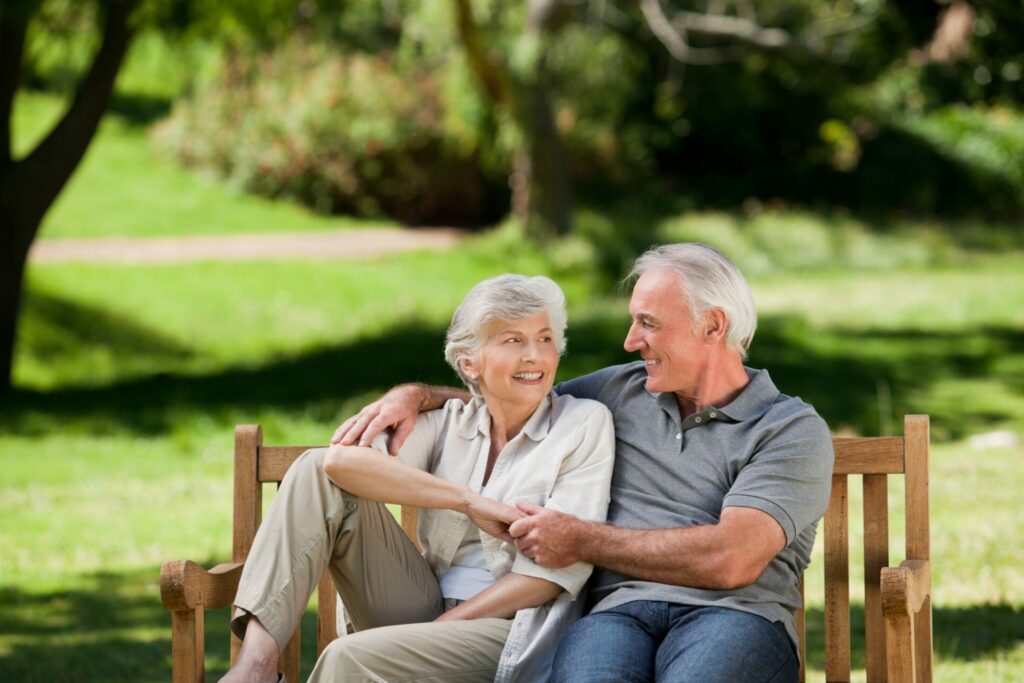 An old couple, enjoying a conversation, sitting on a bench, outdoors.