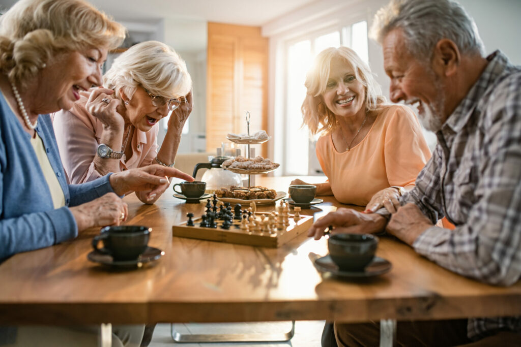 Four people sitting at a table having coffee, and playing chess.