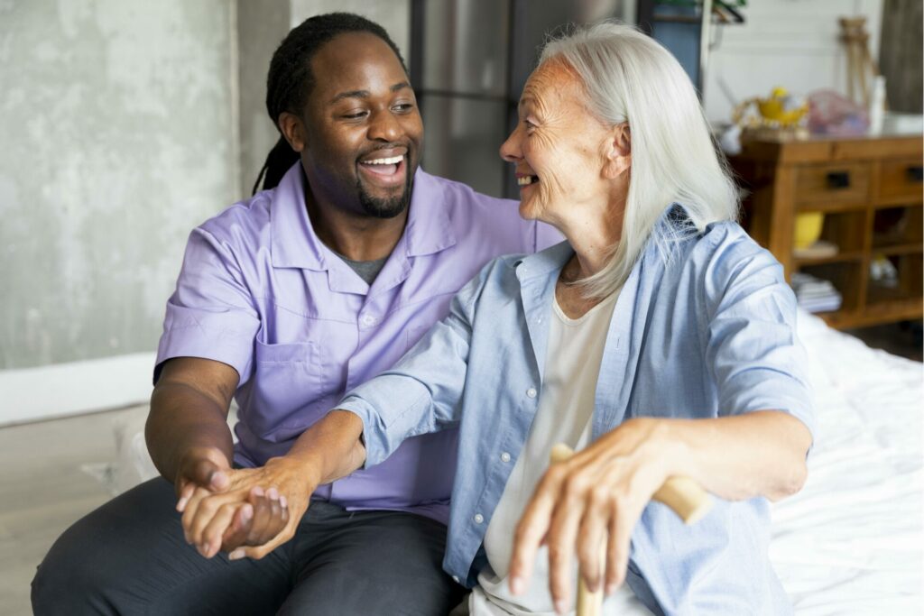 An elderly woman with a big smile on her face, extending her arm, while her hand is being held by a young man, who is helping her extend her arm, with a very friendly smile.