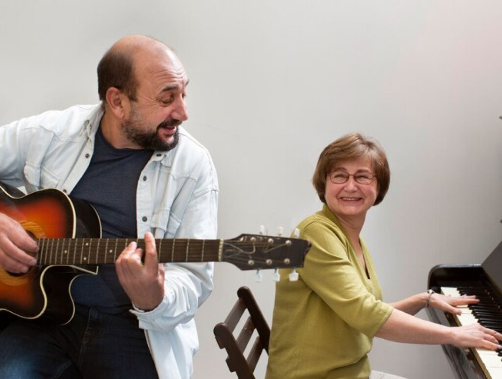 A man playing a guitar while a woman plays the piano.