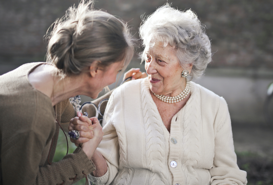 A woman, holding the hand of an elderly woman, both of the woman are smiling.