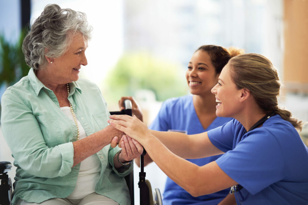 Two nurse's happily assisting an elderly woman.