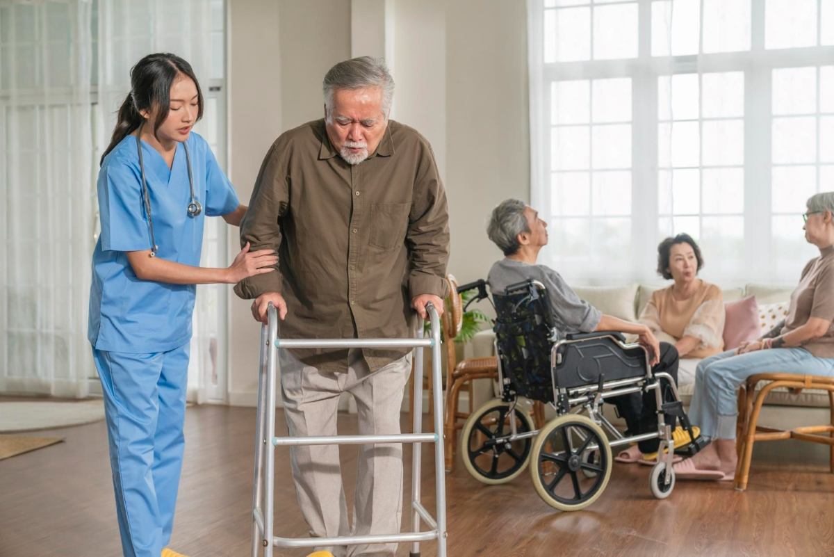 An elderly man with a walking assistance device being helped by a nurse.